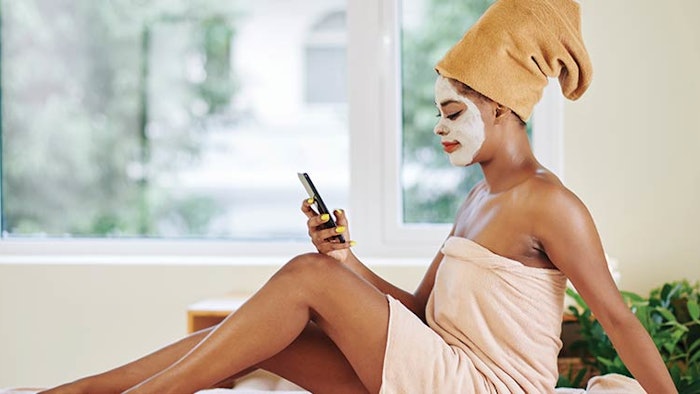 Woman sitting on her phone in a face mask and towel