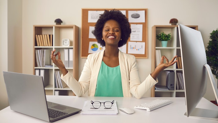 Happy employee getting ready to start productive work day. Young business woman sitting at office desk meditating