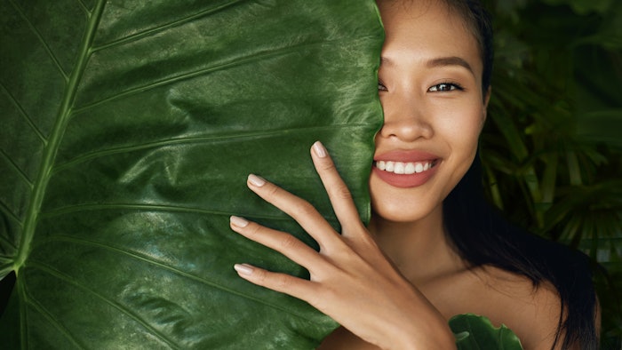 Beauty face. Woman model with natural makeup behind green leaf